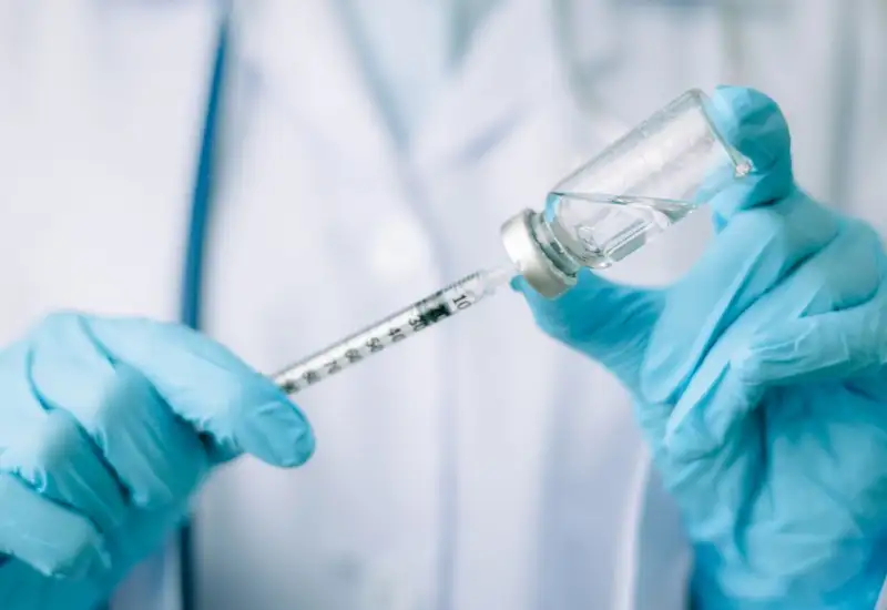 A picture of a doctor drawing out the vaccine with a syringe whilst wearing gloves on both hands