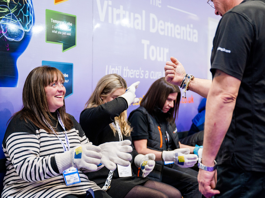 Visitors at the Virtual Dementia Tour experience at Naidex, learning about living with dementia through hands-on demonstrations.