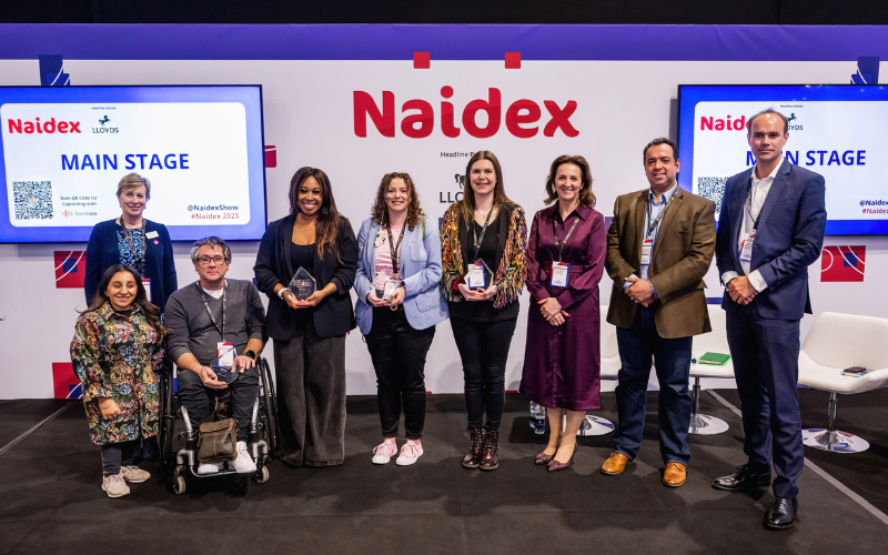 A picture of 9 people on the Naidex main stage for the Elevate awards, they are smiling into the camera.