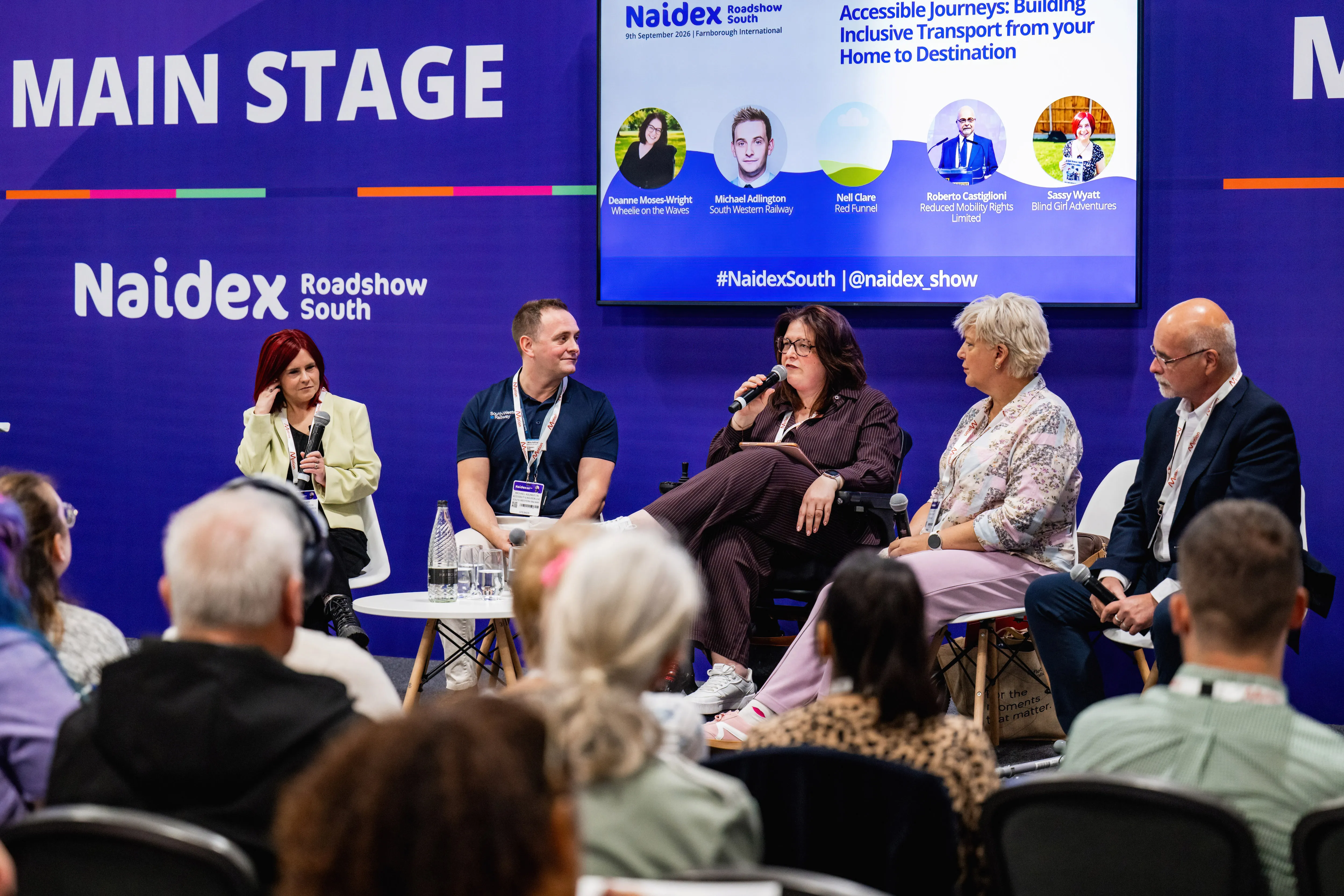 A group of exhibitors and attendees posing together in front of the ‘Village Green’ backdrop at Naidex.