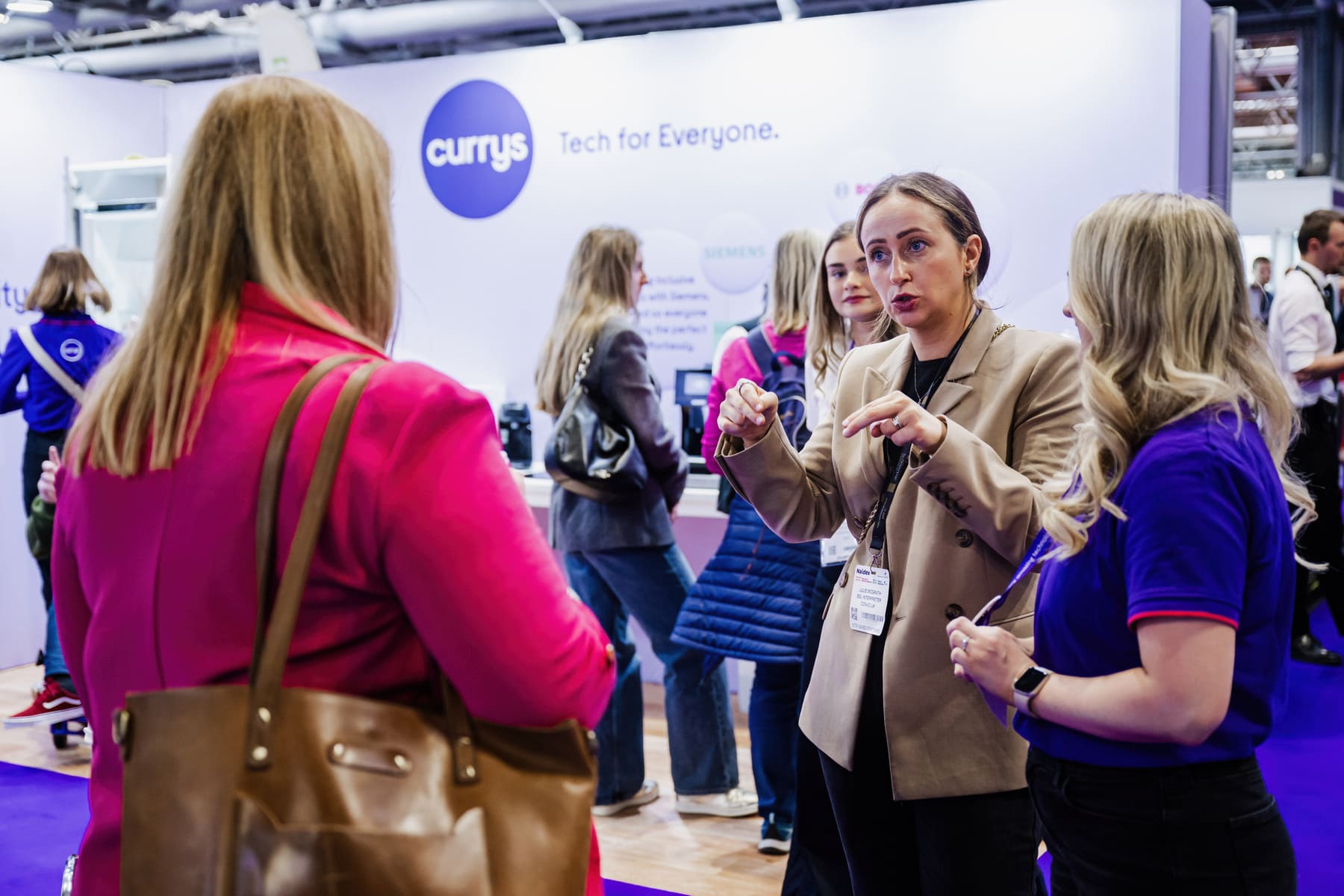 Three women smiling and taking a selfie in front of a large ‘Welcome to Naidex’ display at the event entrance.
