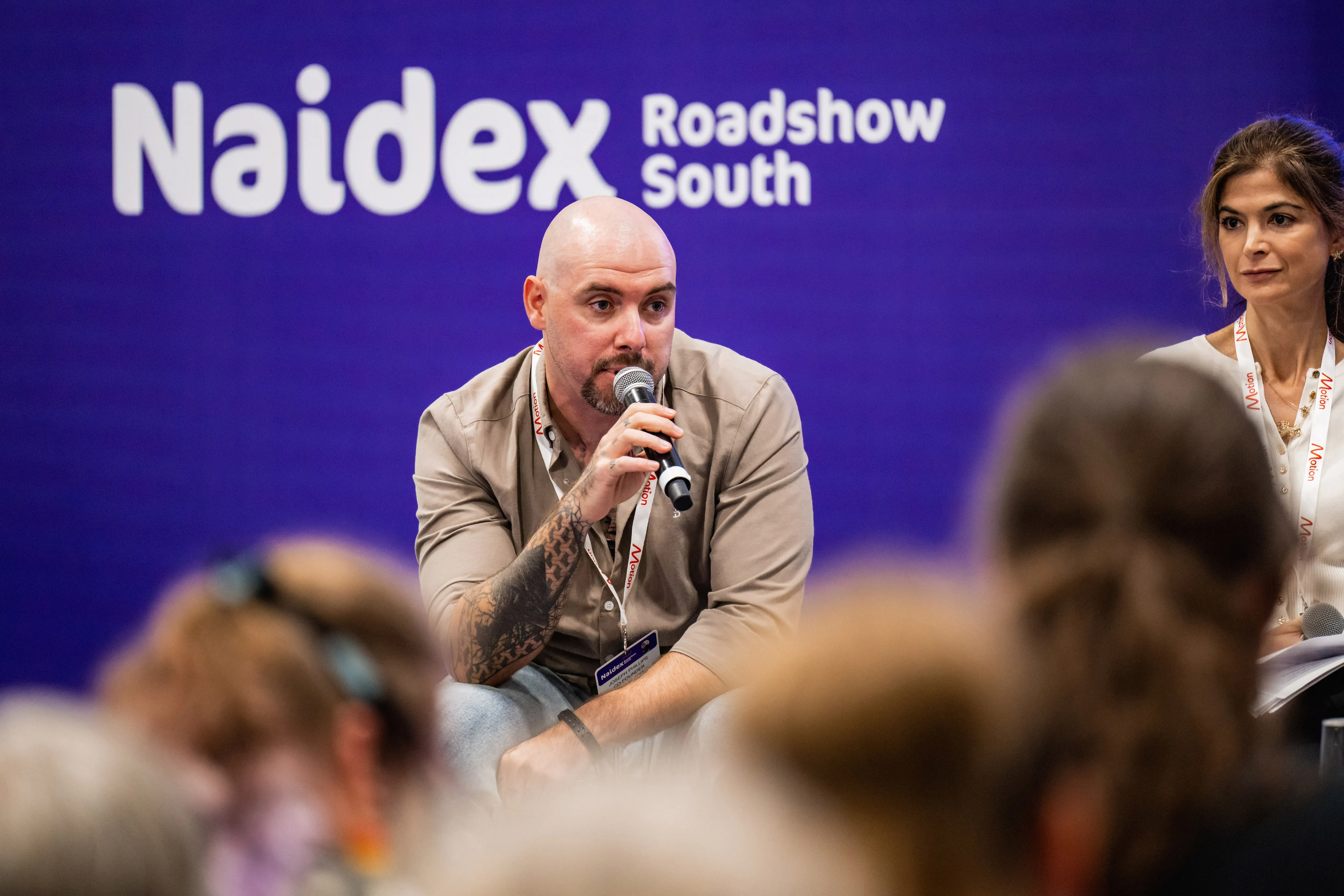 “Paralympian Richard Whitehead speaking on stage at Naidex, standing beside a screen showing his athletic achievements.