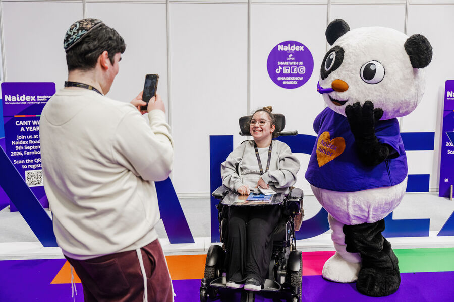 “Paralympian Richard Whitehead speaking on stage at Naidex, standing beside a screen showing his athletic achievements.