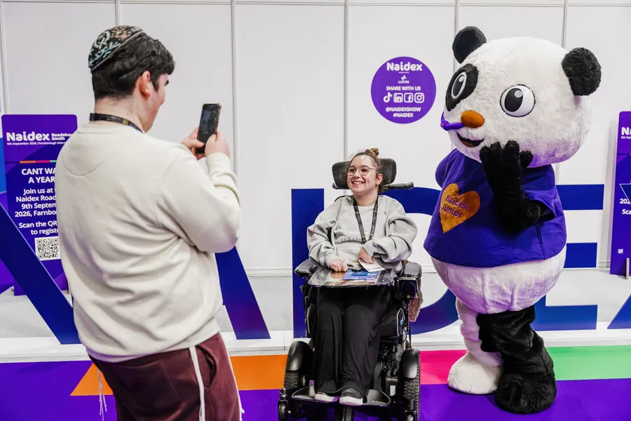 “Paralympian Richard Whitehead speaking on stage at Naidex, standing beside a screen showing his athletic achievements.