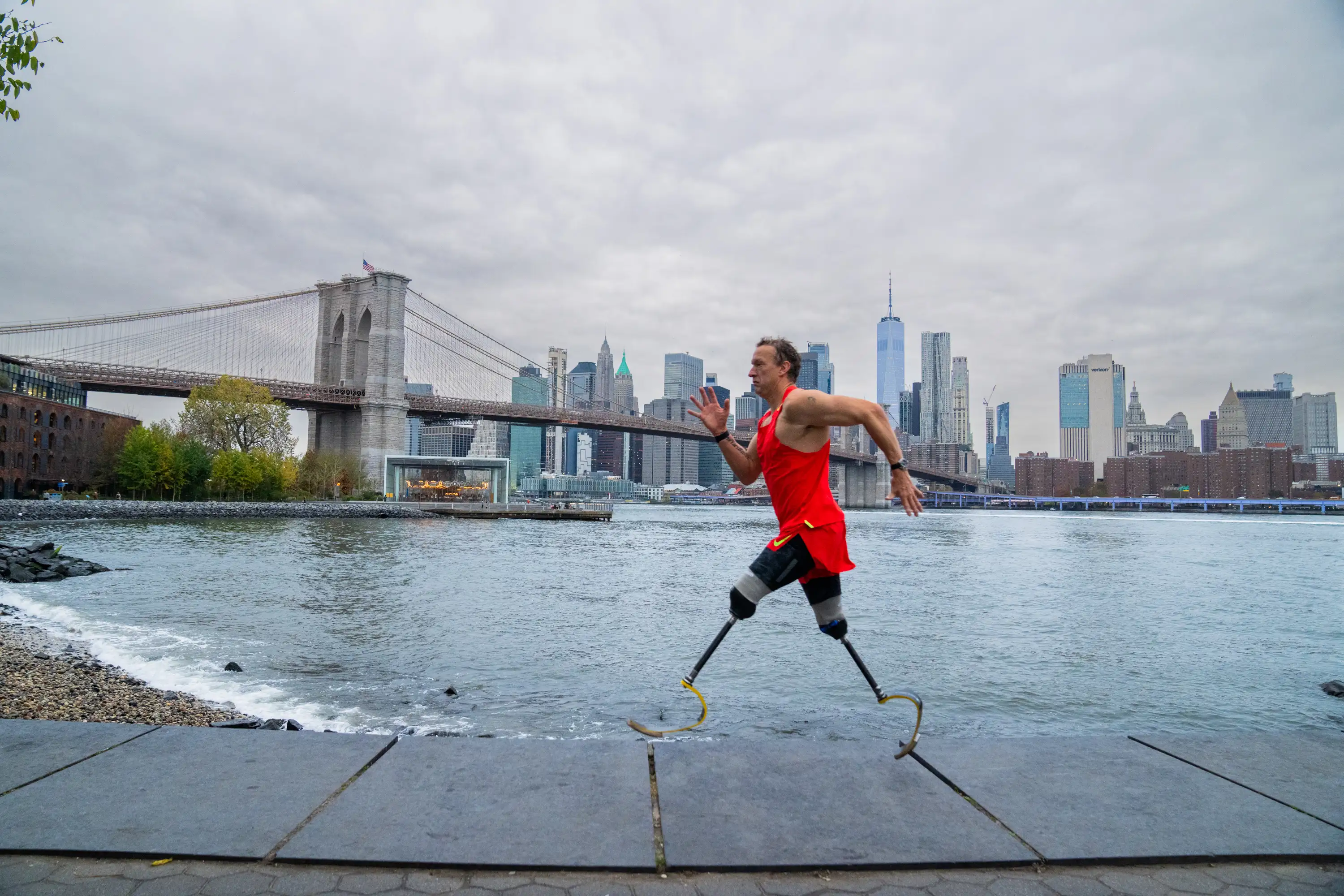 A picture of Stephen Whitehead running along the New York river, he is wearing a long bright orange vest. 