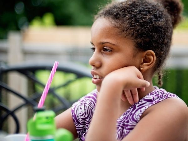An image of a girl sat down outside leaning her head on her hand 