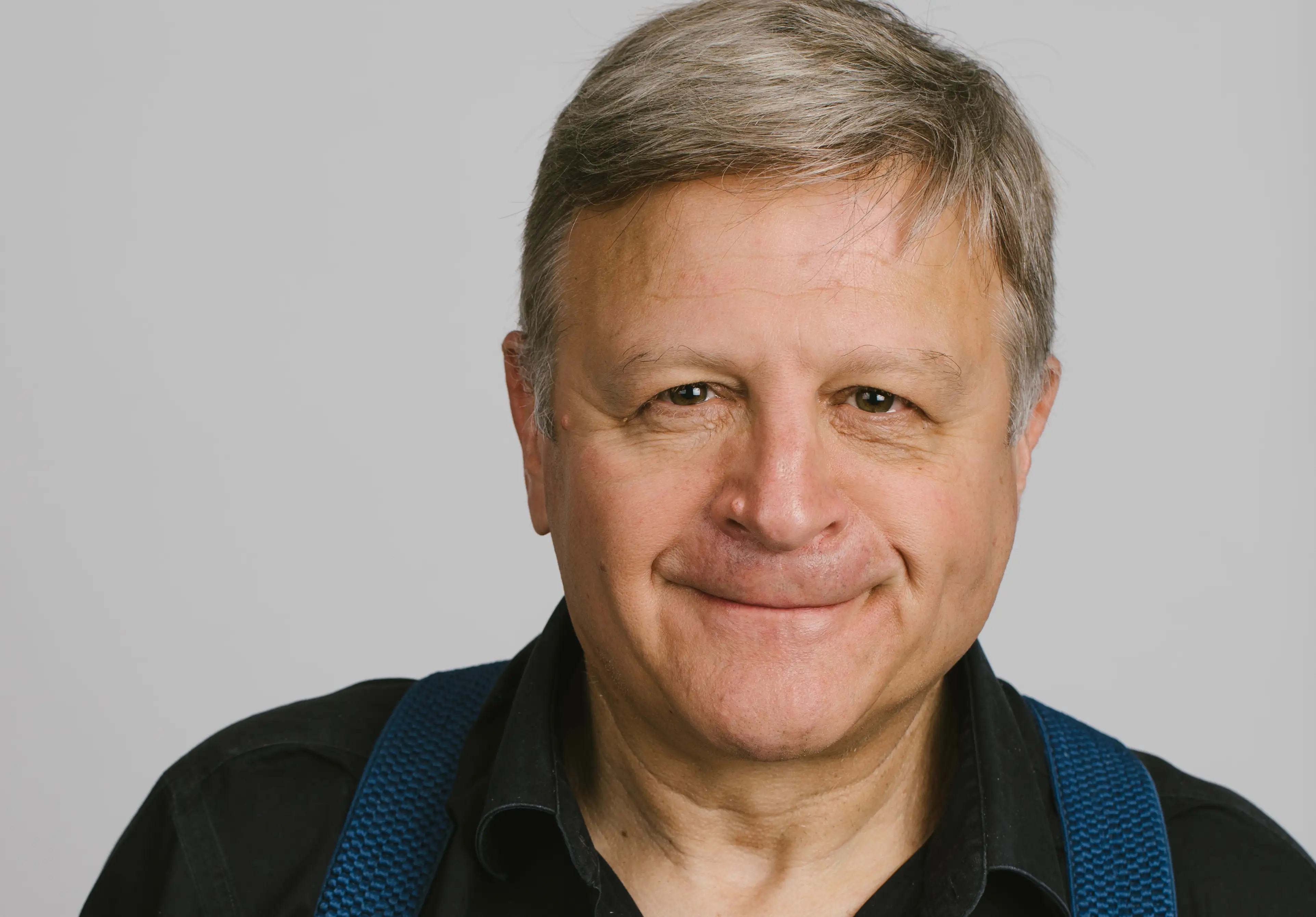 Daniel Casson from the waist up, smiling to the camera wearing a black shirt. 