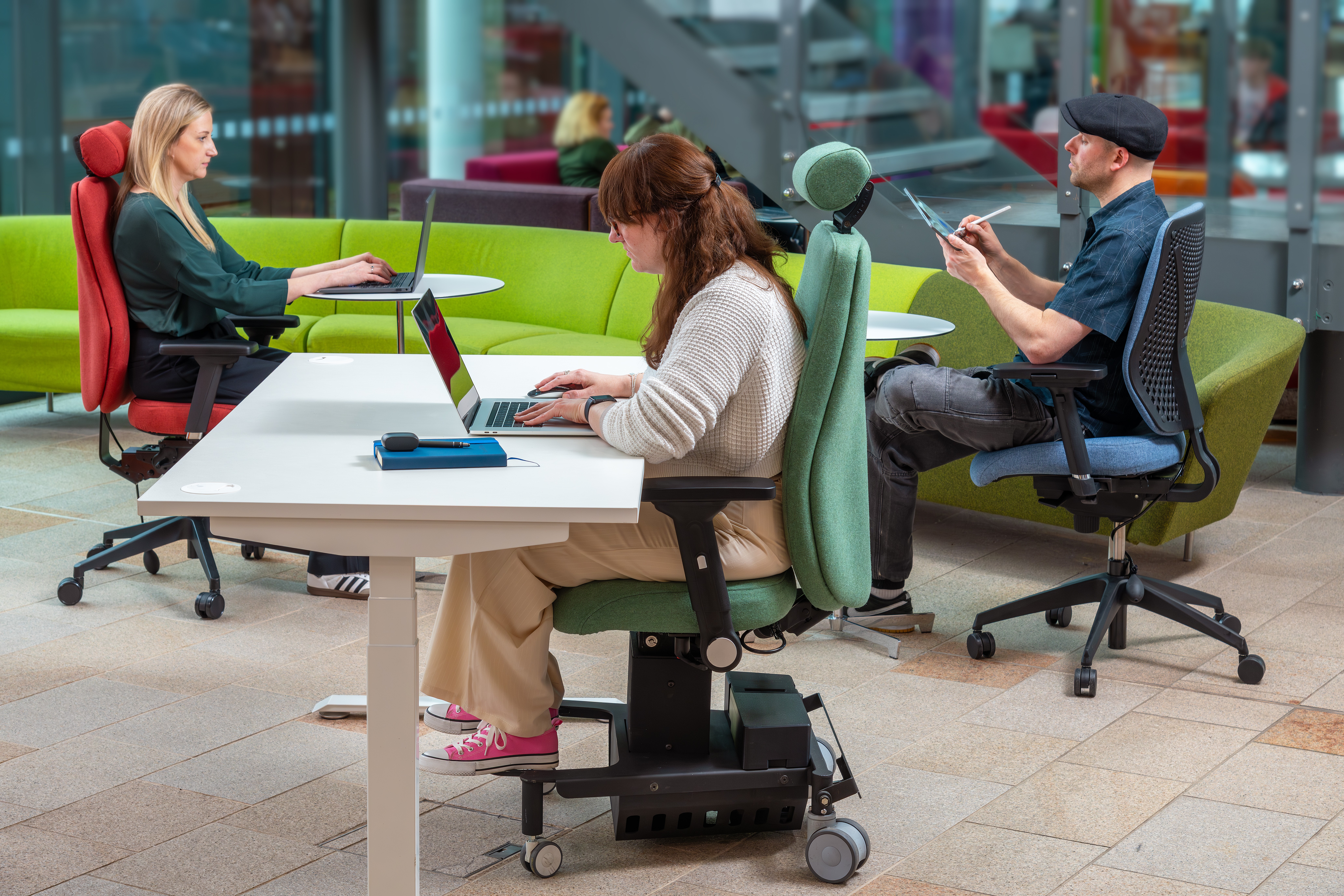 A picture of three people in an office sat at desks working on laptops 