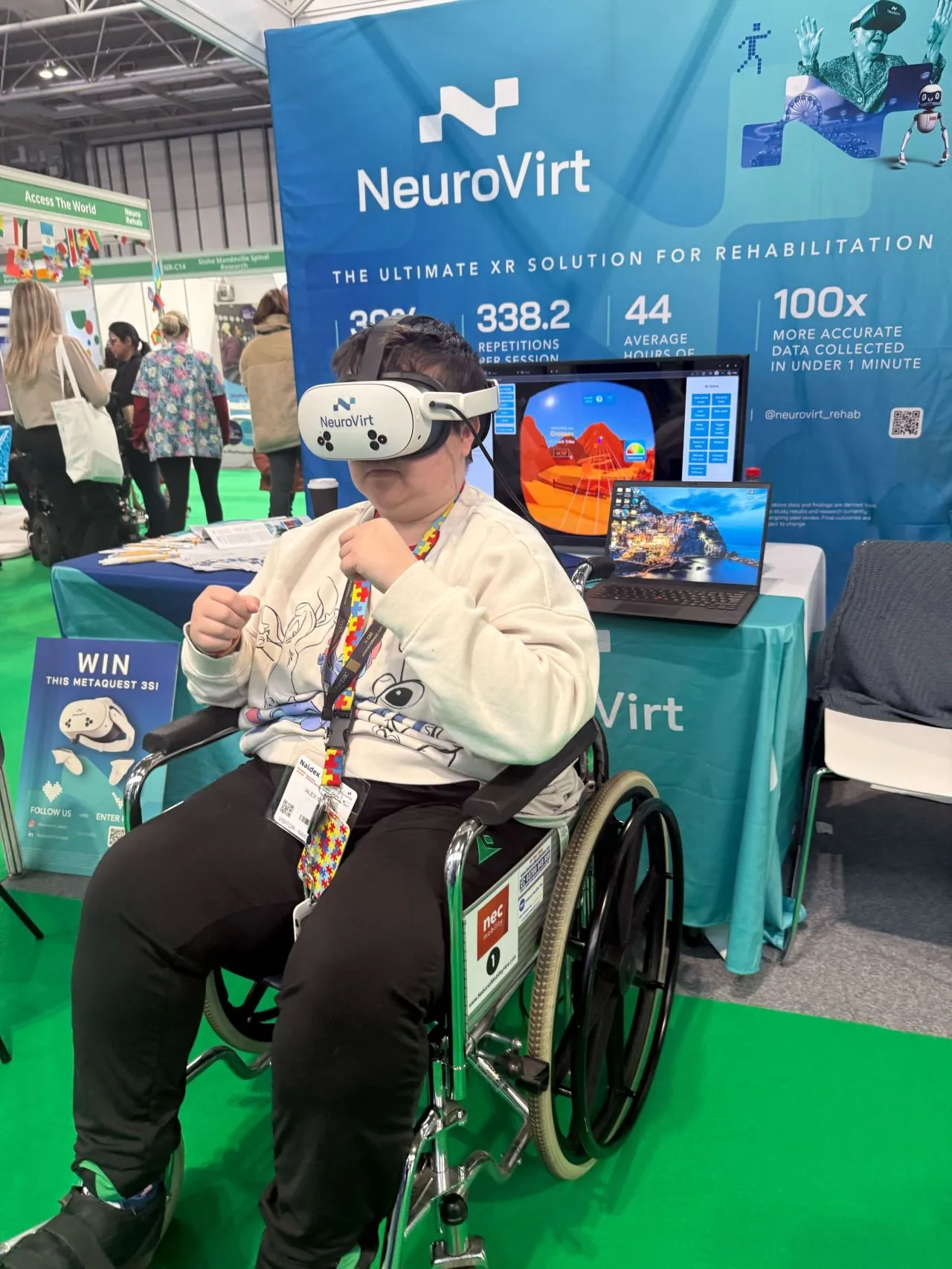 A person using a VR headset while seated in a wheelchair at an exhibition stand, with NeuroVirt branding and screens displaying rehabilitation technology in the background.