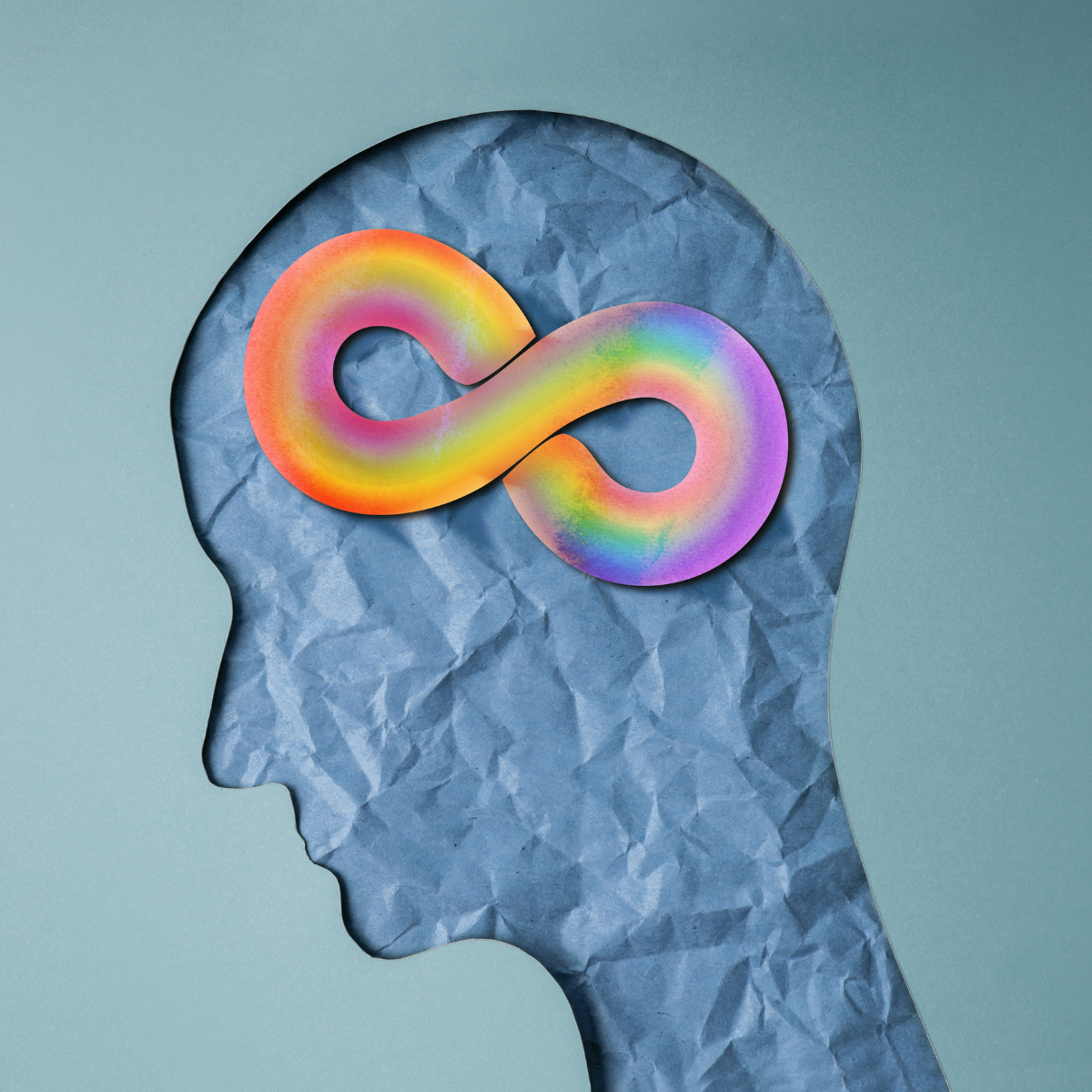 A stylised illustration of a human head in profile, shown as a crumpled blue paper texture, with a colourful rainbow infinity symbol positioned inside the brain area against a soft gradient background.
